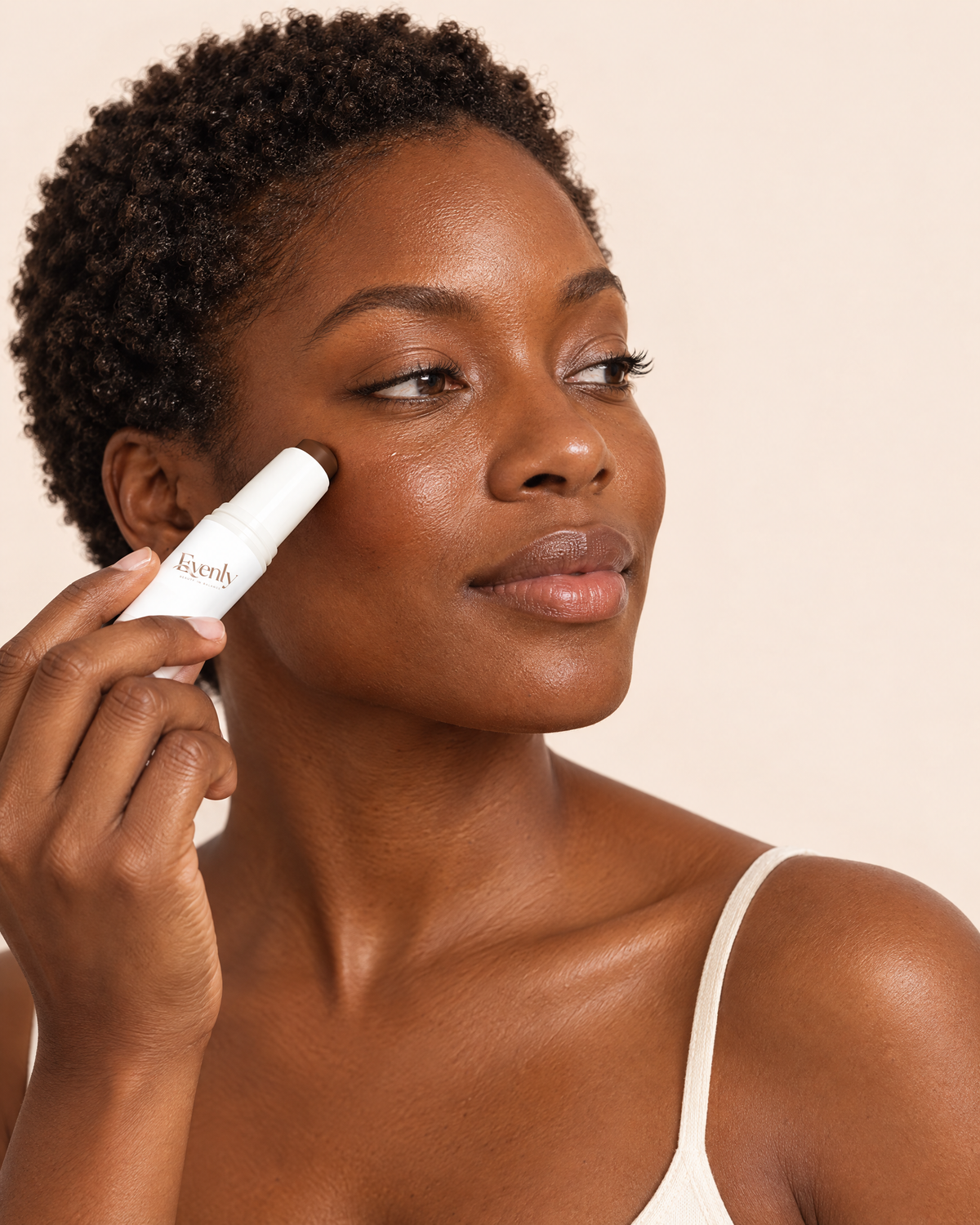 Woman with deep brown skin applying the Evenly Day Stick to her cheekbone