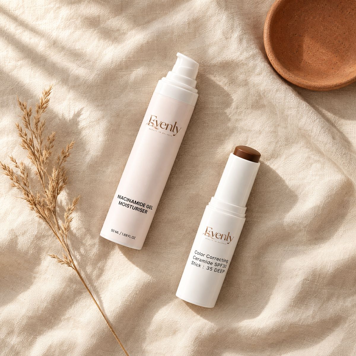 Evenly Night Cream and Day Stick laid on warm cream linen with dried grass and a terracotta dish